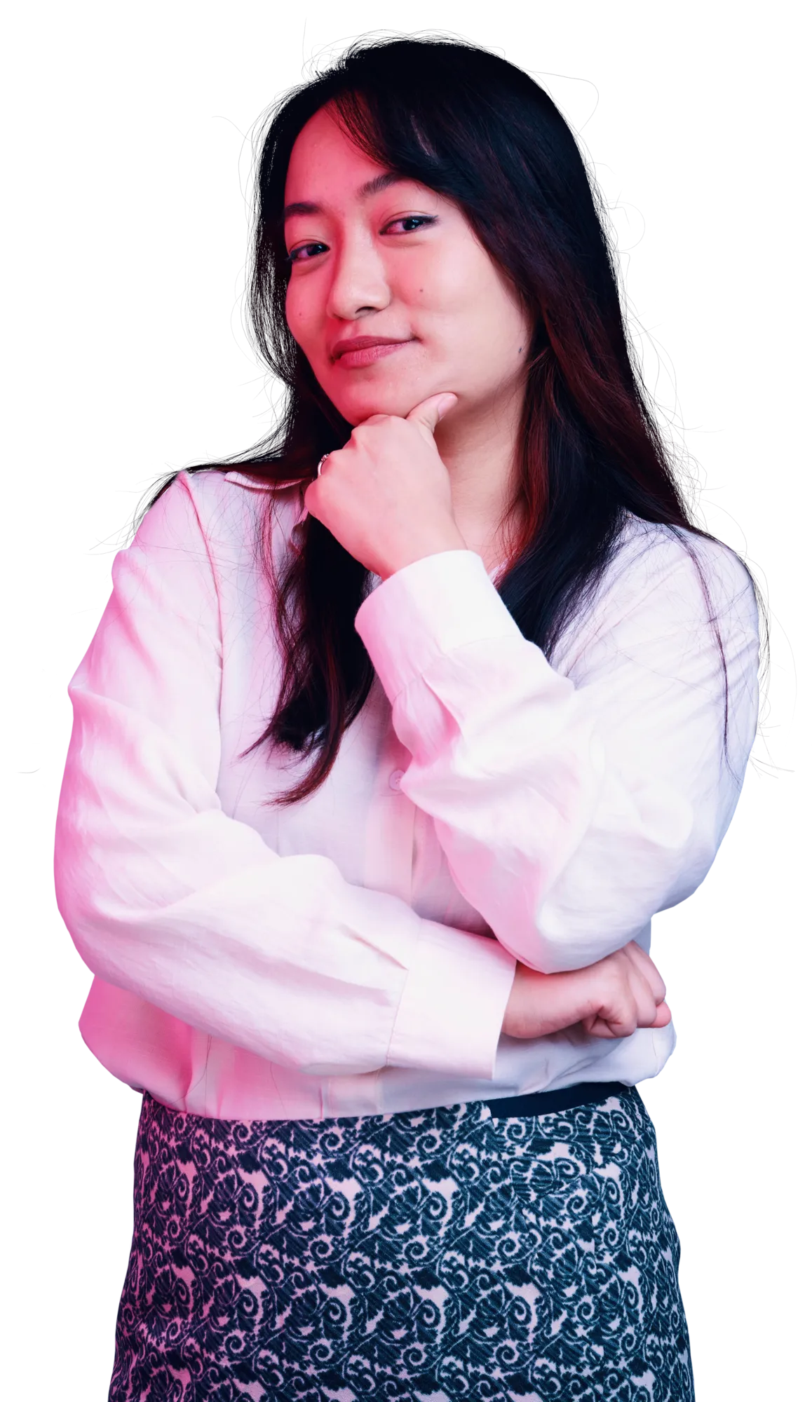 A woman with long dark hair wearing a white sweater and a patterned skirt poses with her hand on her chin.