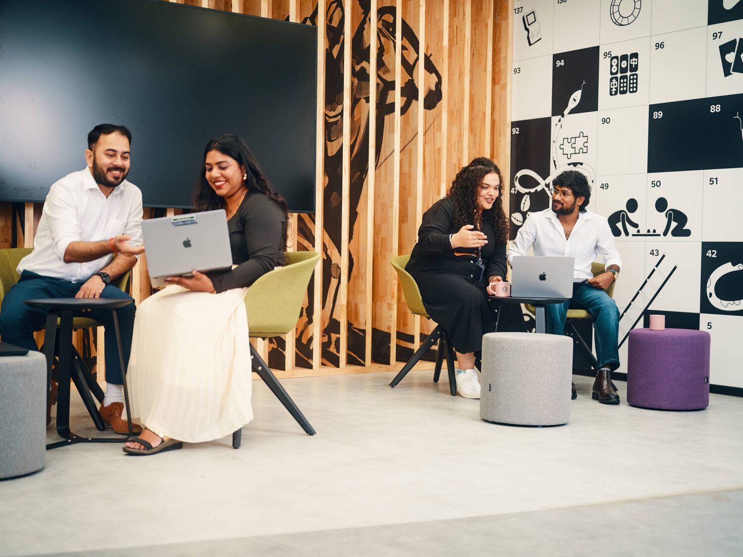 Four people work on laptops at small tables in a modern coworking space with a wooden slat divider and a black-and-white patterned wall.