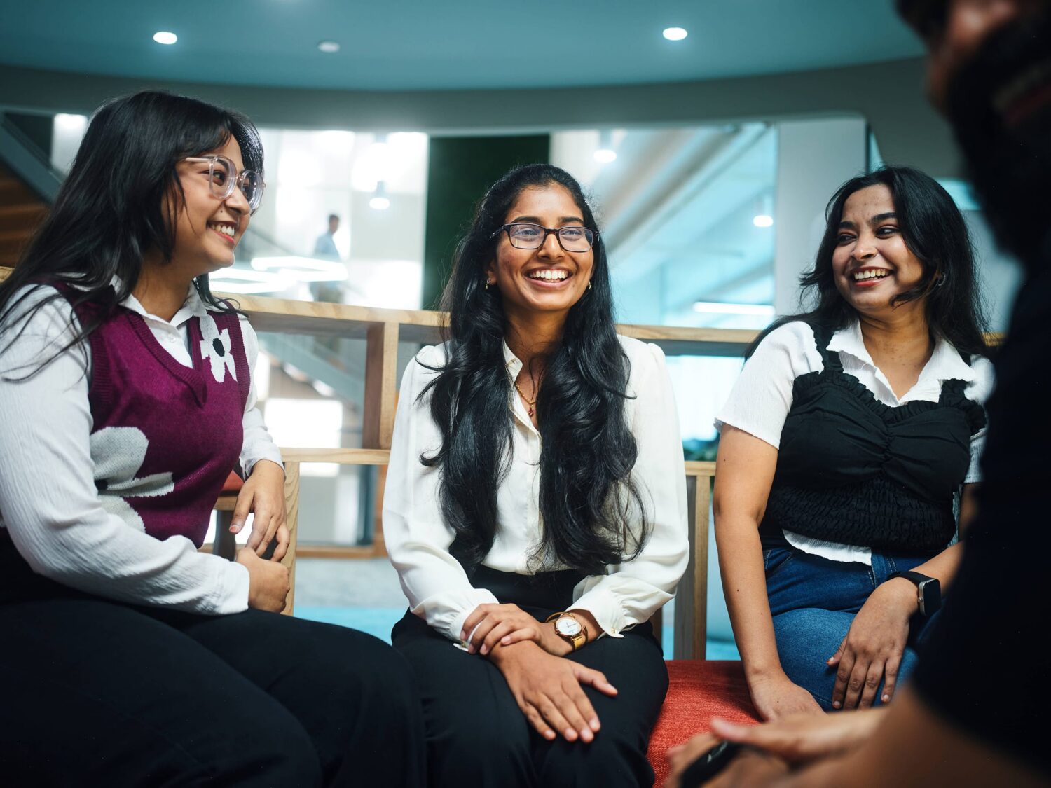 Three women sit together and smile in a bright, modern office or coworking space.