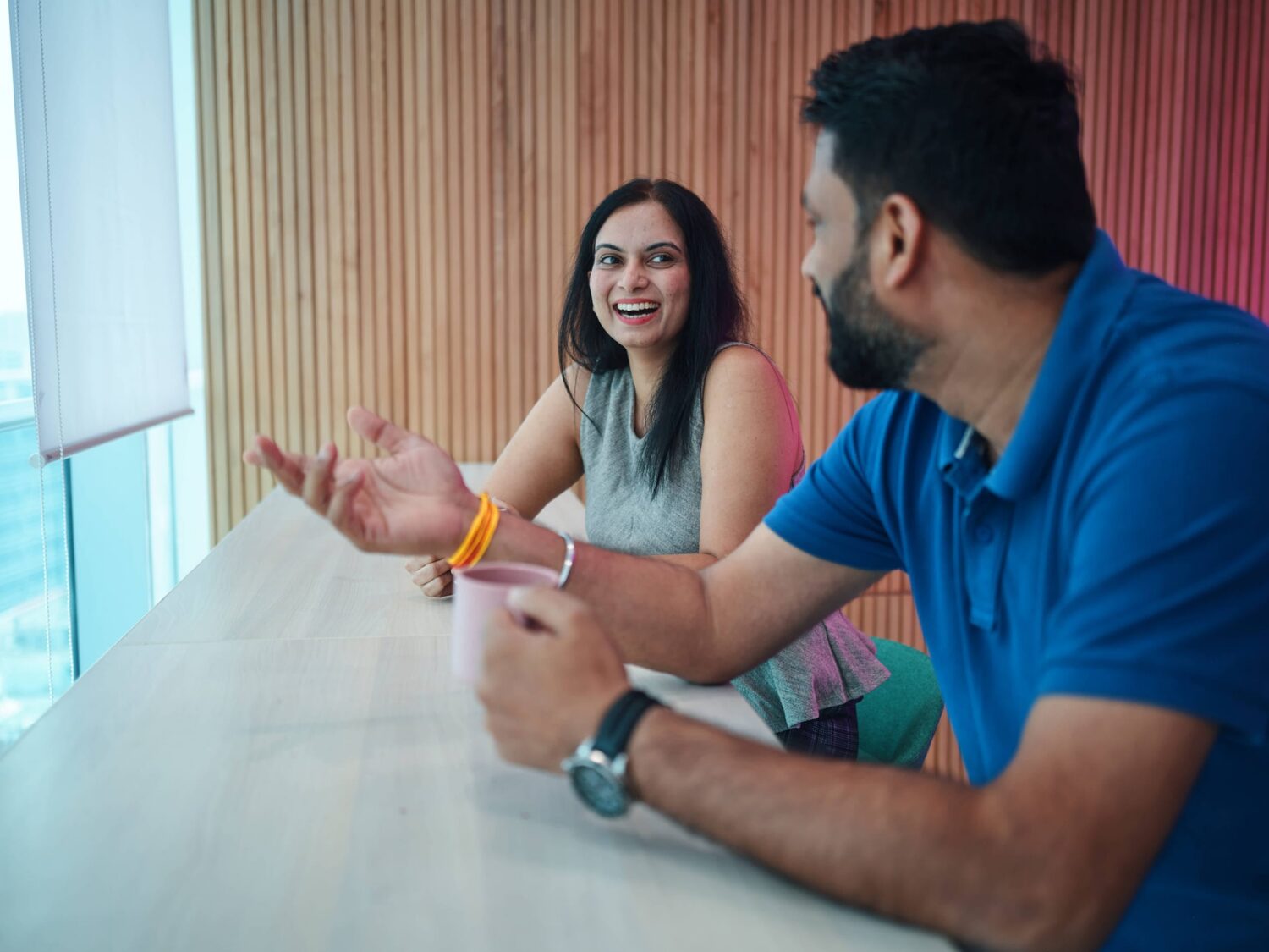 Two people sit at a white table by a window, smiling and talking.