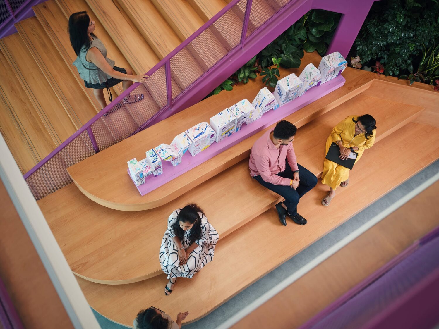 Overhead view of a wooden playground slide with purple rails, where several people are seated and walking along a curved platform.
