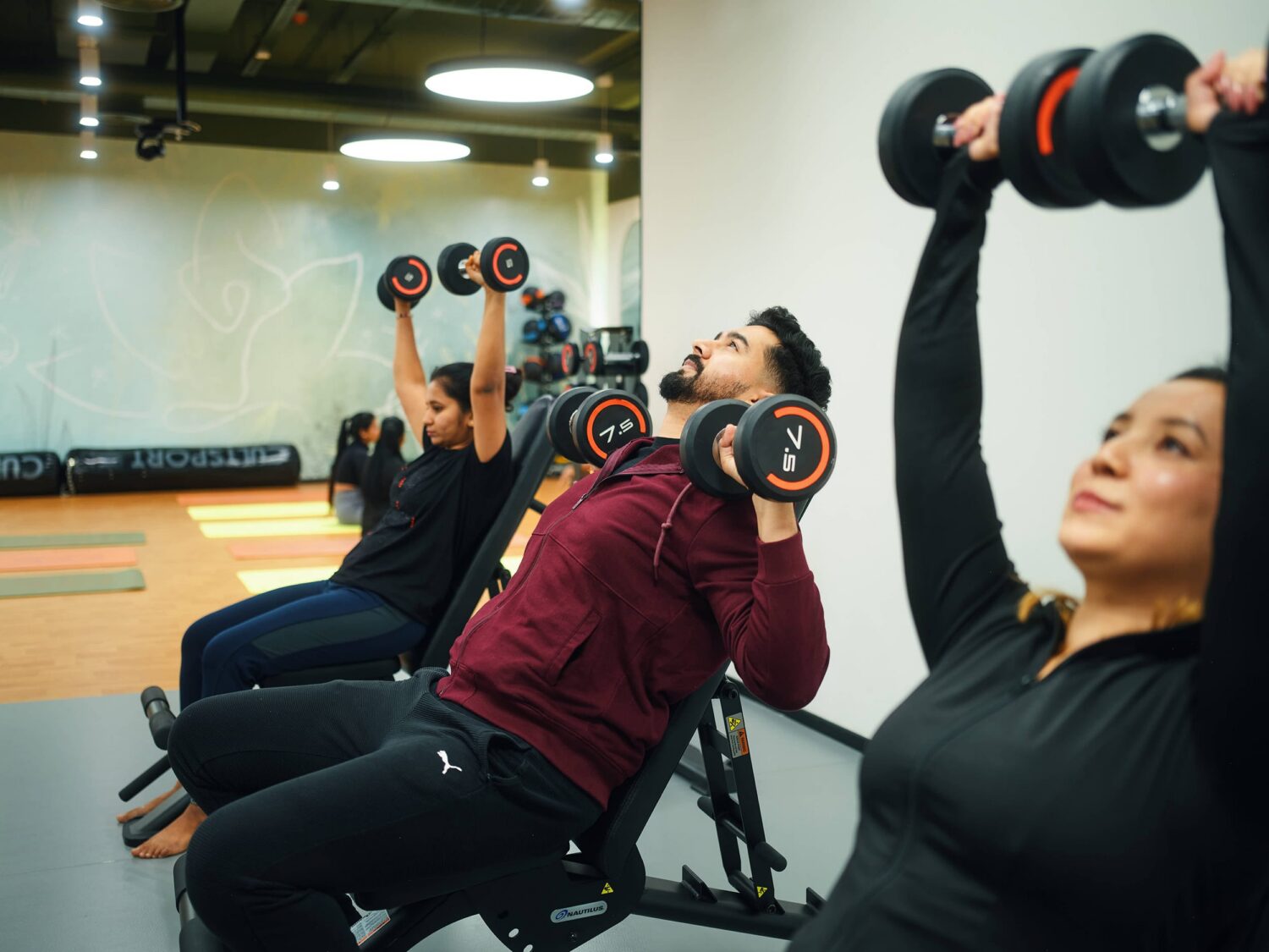 Several people in a gym performing incline bench dumbbell presses.