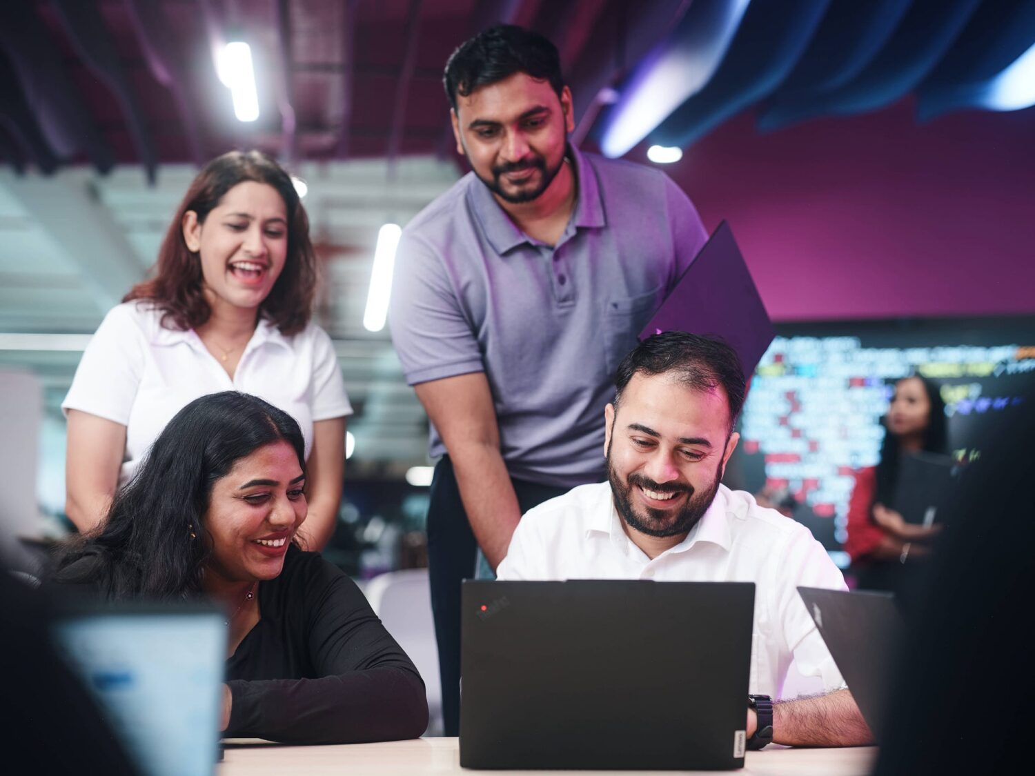 A diverse group of coworkers collaborates around a table with laptops in a modern office.